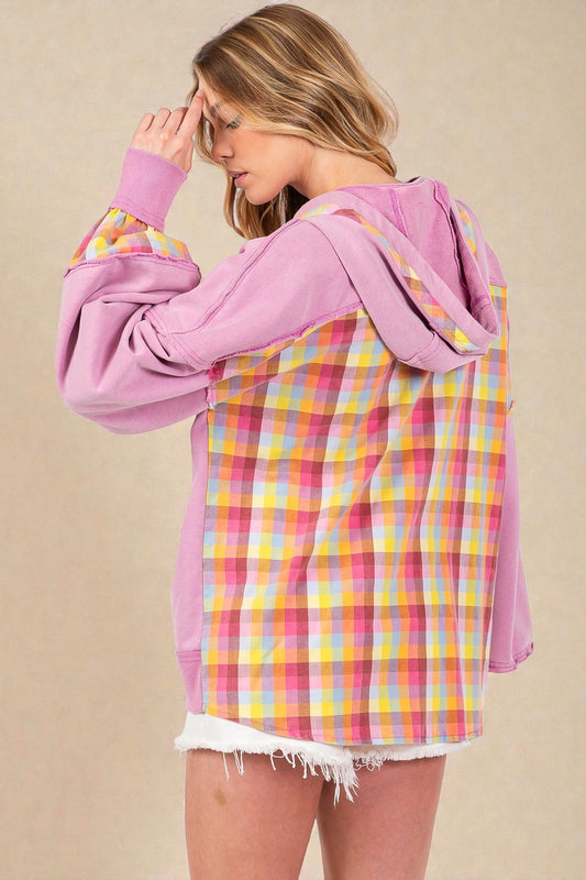 Person wearing a pink hoodie with a colorful plaid shirt underneath on a beige background