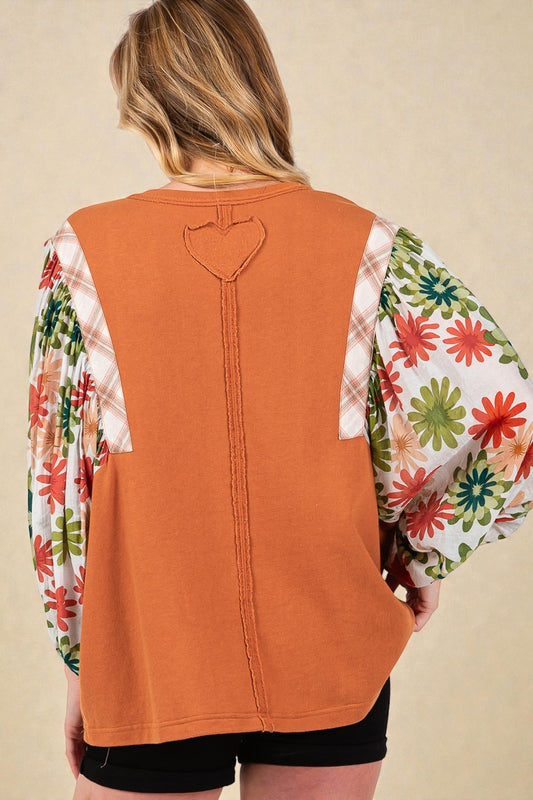 Person wearing a rust-colored vest over a colorful floral shirt on a beige background