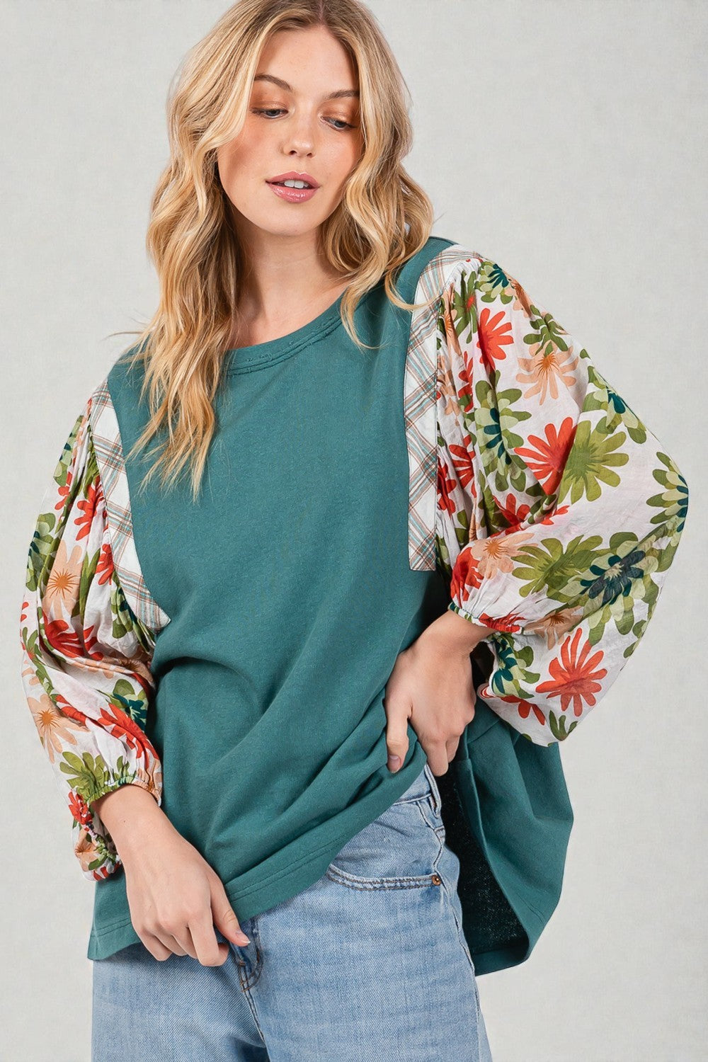 Woman wearing a teal sweater with floral sleeves against a plain background