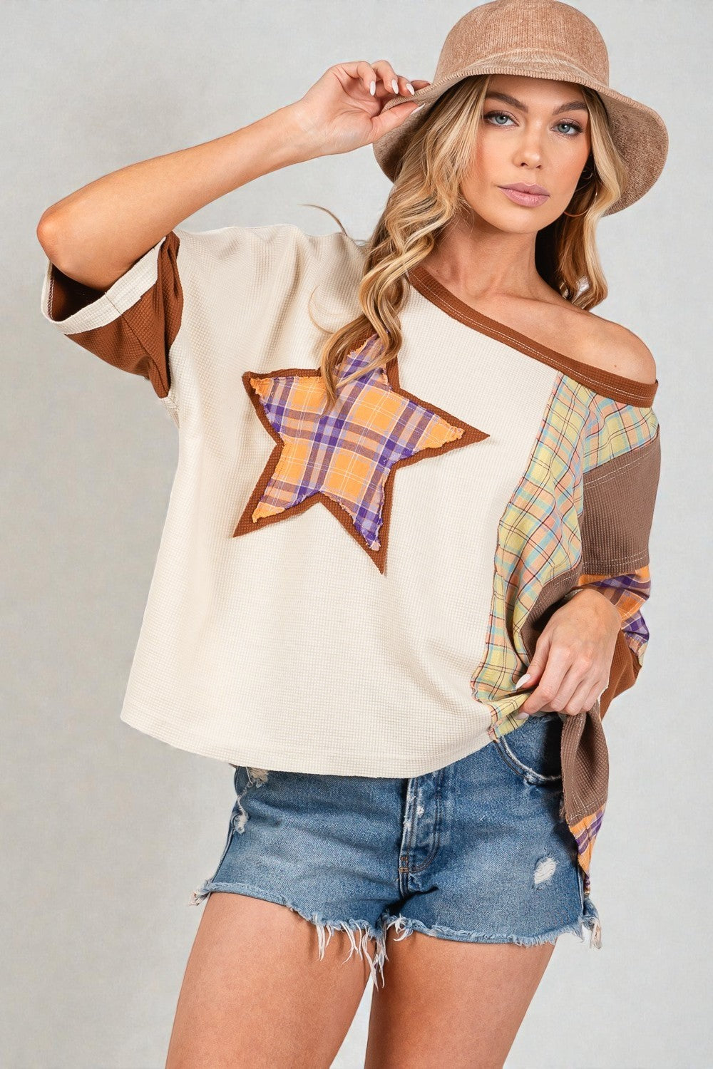 Woman wearing a cream-colored top with star design and denim shorts on a plain background