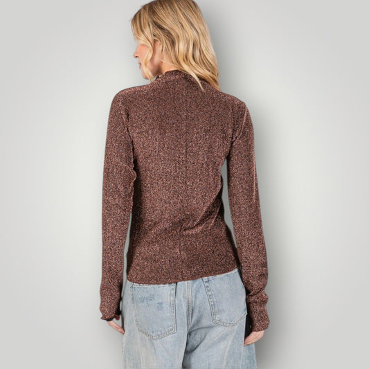 Person wearing a brown knitted sweater and light blue jeans against a plain background