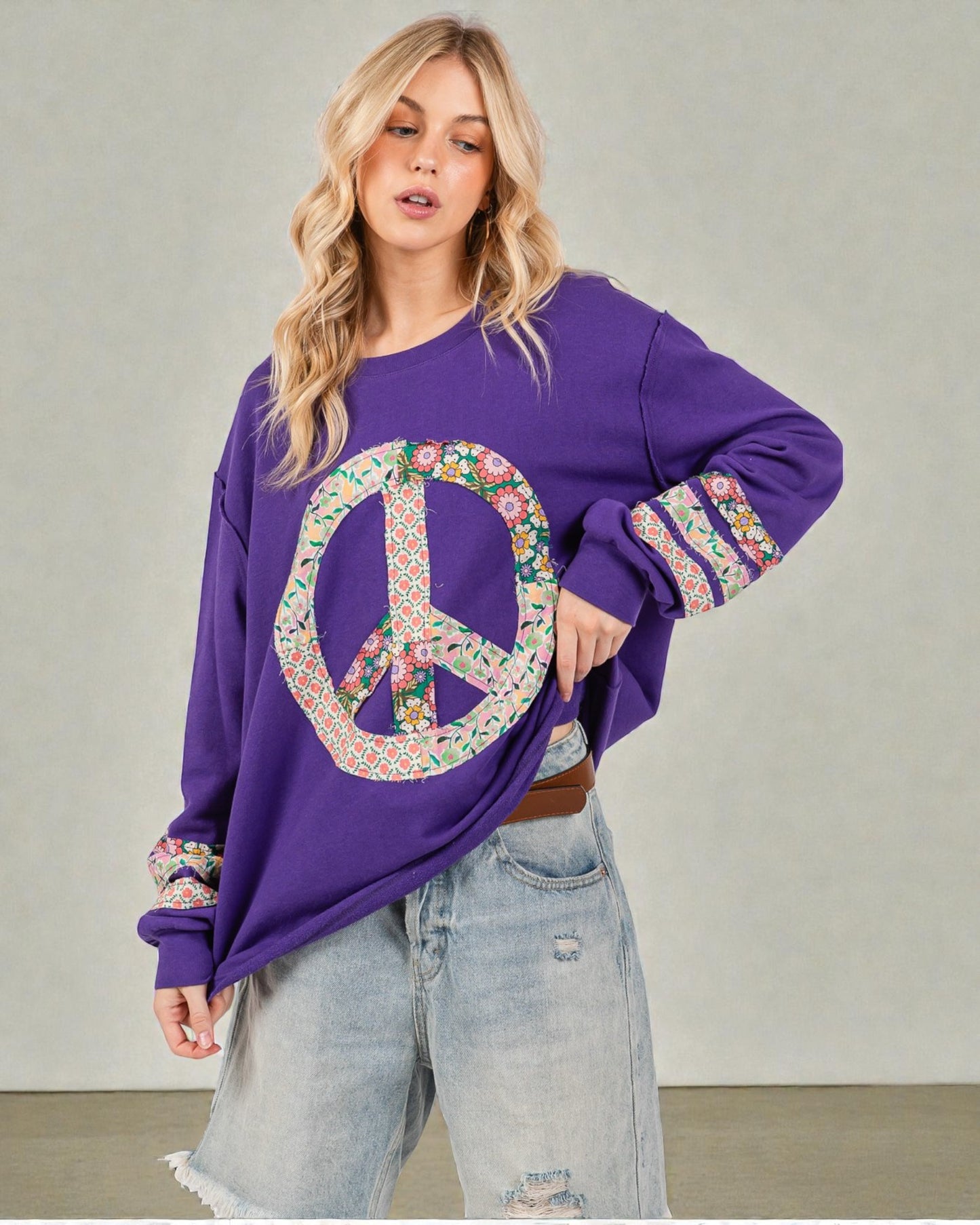Woman wearing a purple sweatshirt with a peace symbol design, standing against a plain background.