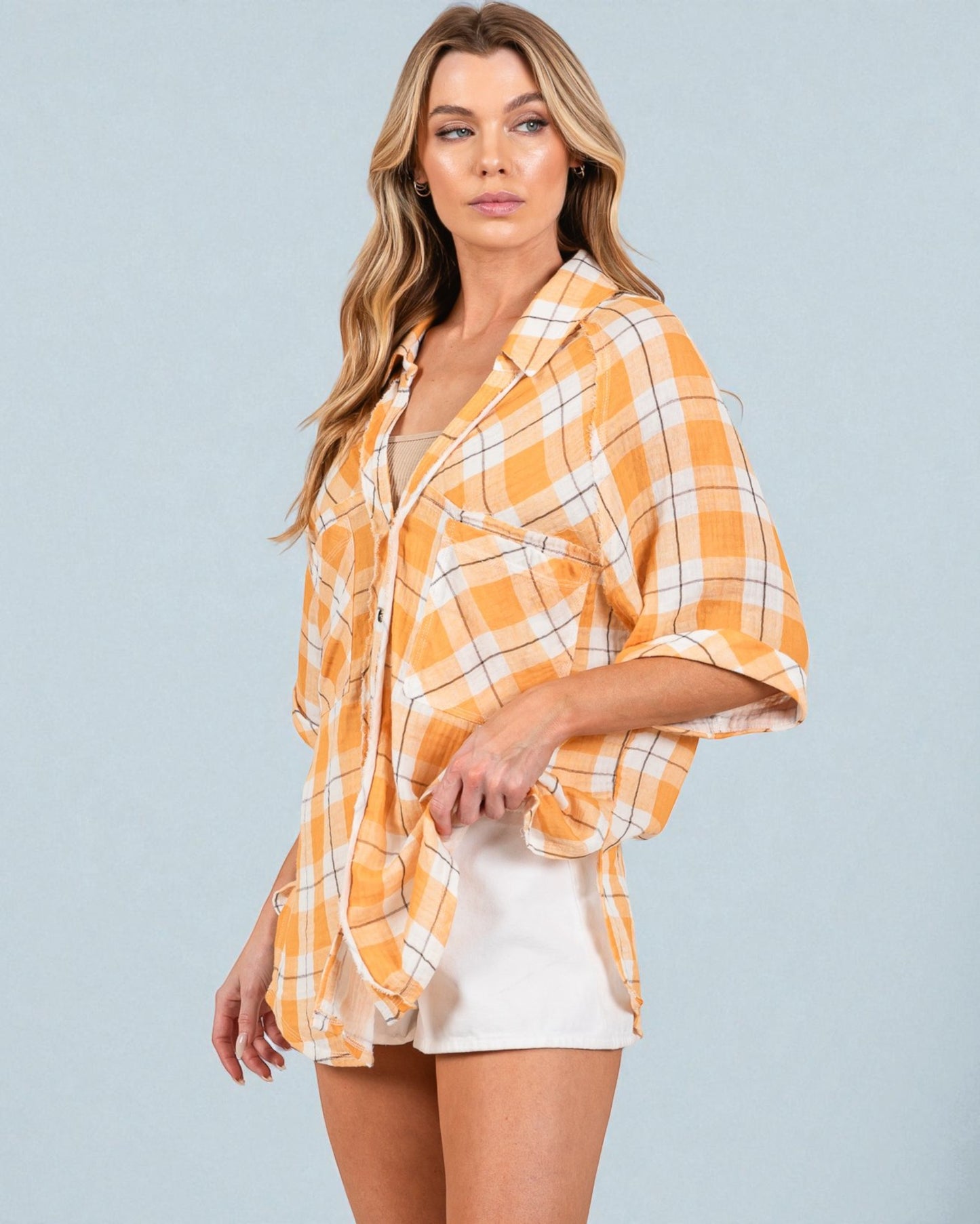 Woman wearing a yellow plaid shirt over a white top with beige shorts on a gray background