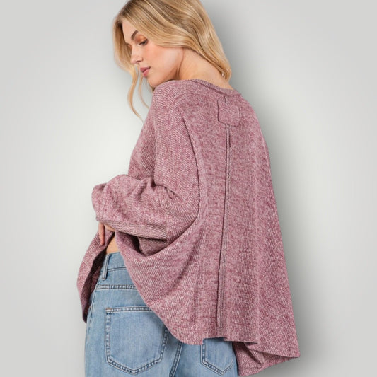 Woman wearing a pink knitted cardigan and blue jeans against a plain background