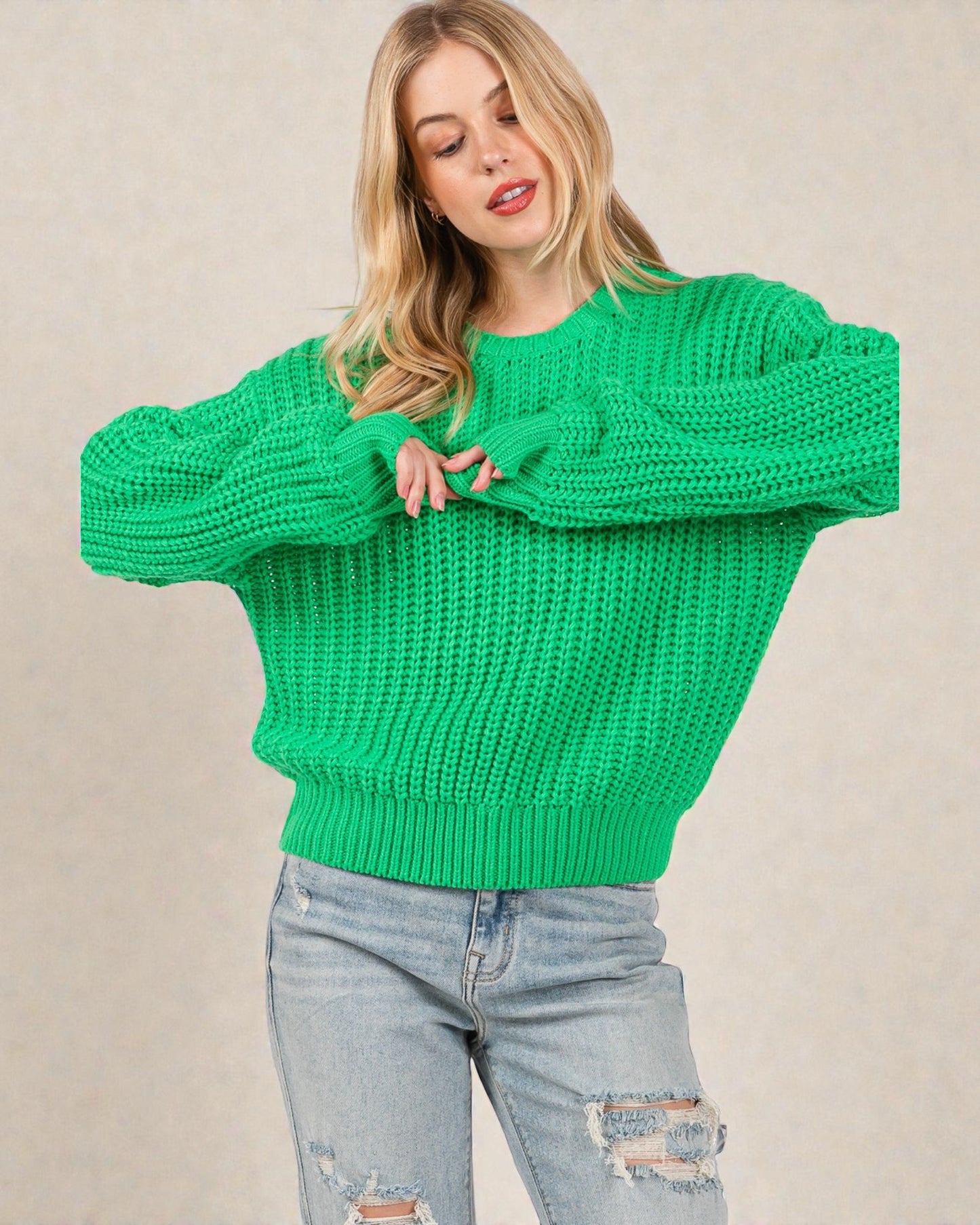 Woman wearing a green knitted sweater and light blue jeans against a beige background