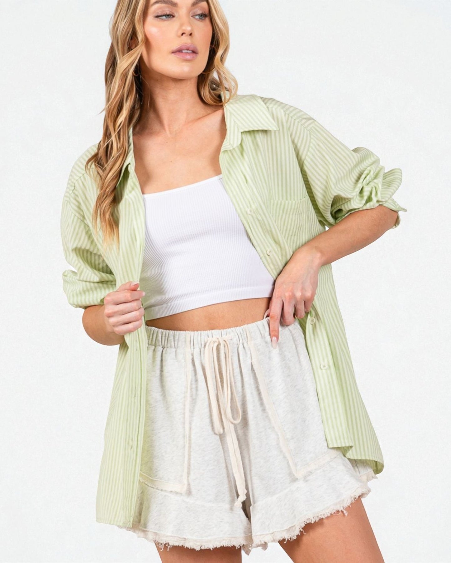 Woman wearing a light green striped shirt over a white top and shorts on a white background