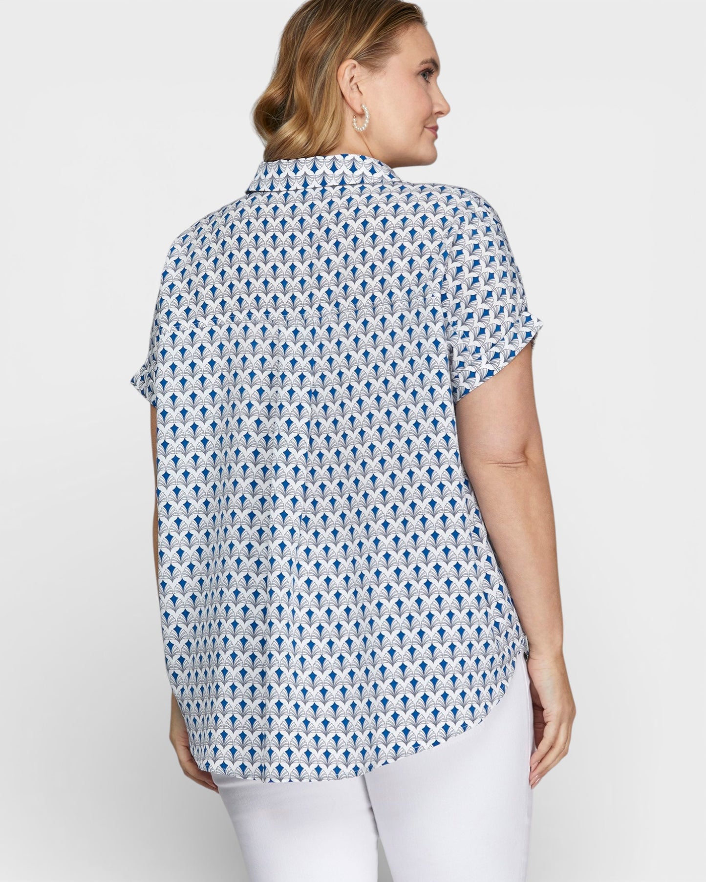 Woman wearing a blue patterned shirt and white pants on a plain background