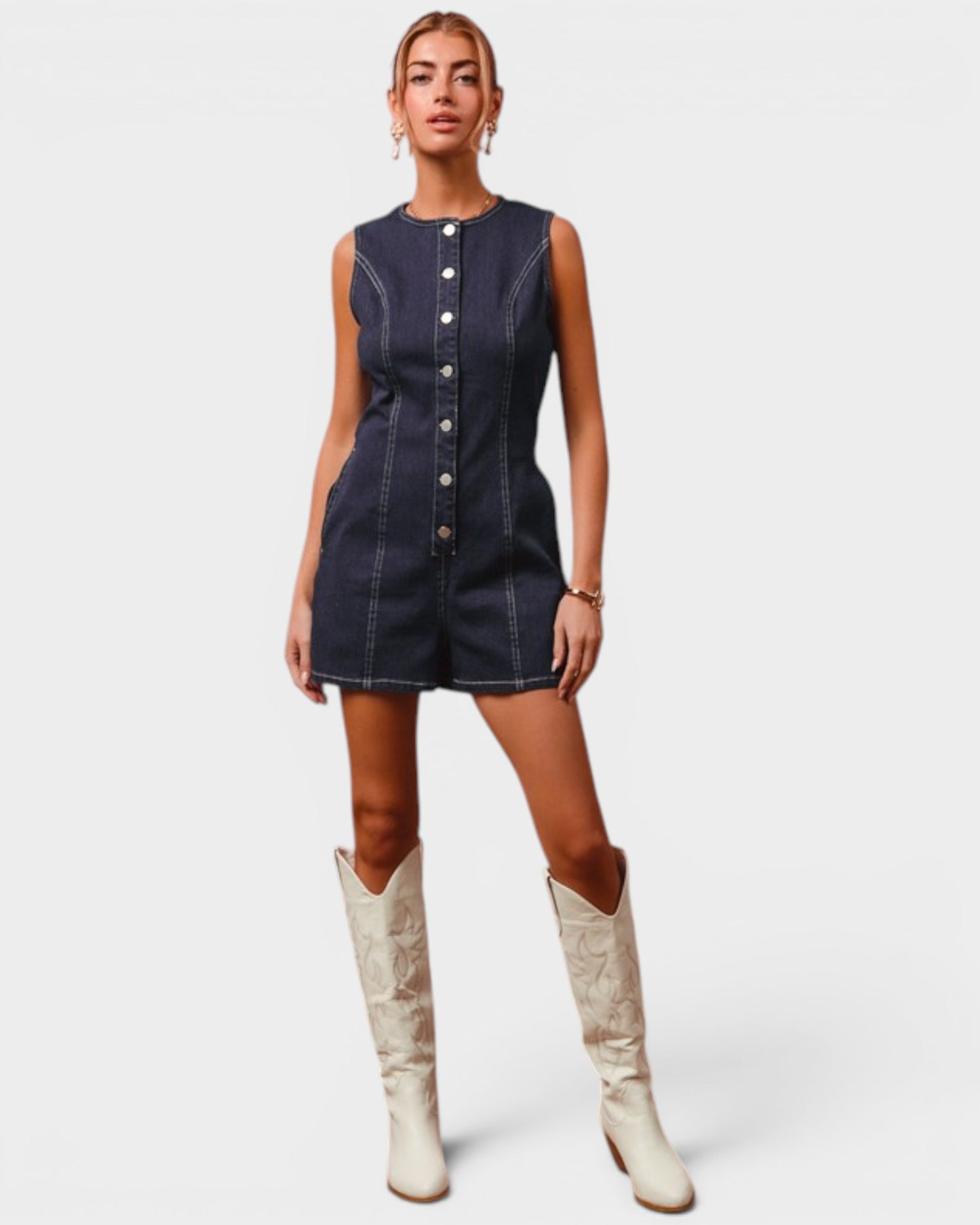 Woman wearing a denim romper and white boots on a plain background
