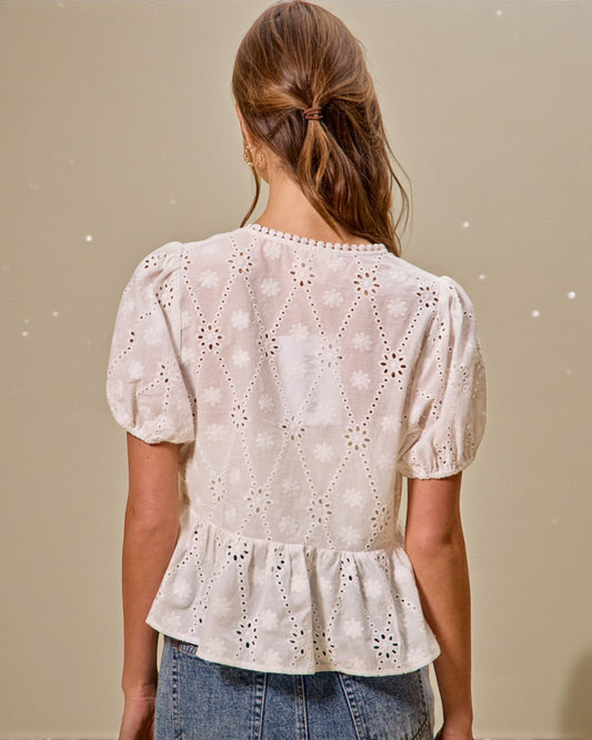 Woman wearing a white lace blouse with puffed sleeves against a beige background