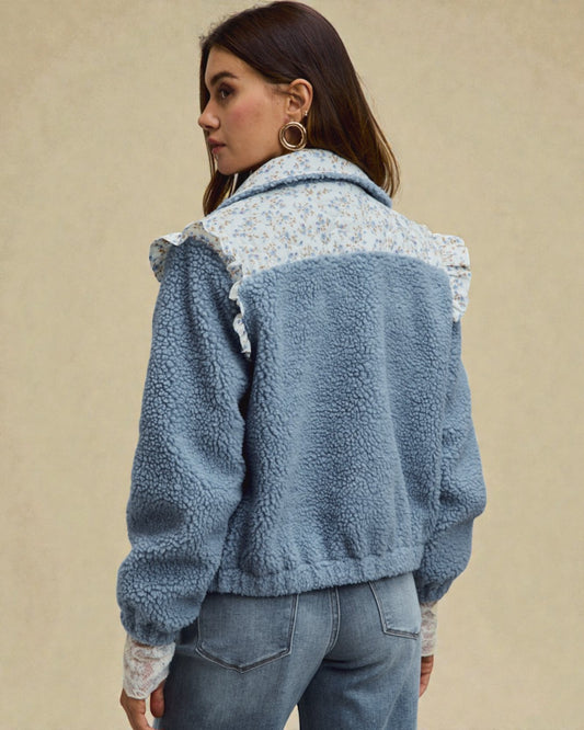 Woman wearing a blue fleece jacket with floral patterned lining on a beige background