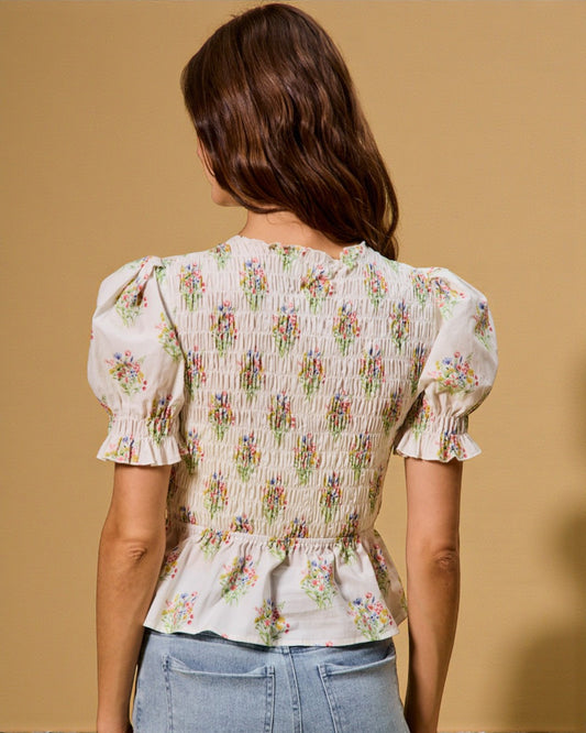 Woman wearing a floral blouse with puffed sleeves against a beige background