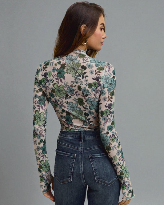 Woman wearing a floral long-sleeve top and jeans on a gray background