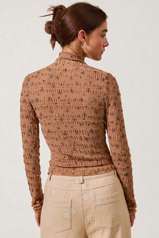 Woman wearing a patterned brown top and beige pants on a white background