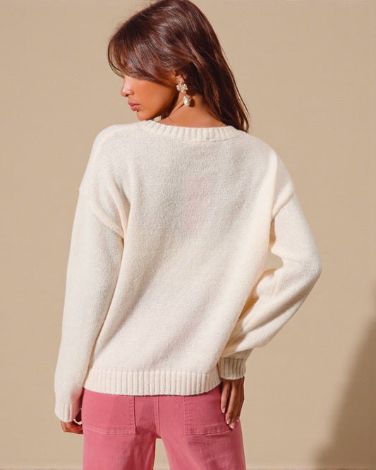 Woman wearing a cream sweater and pink pants against a beige background