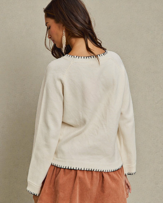 Woman wearing a cream sweater with decorative trim on a beige background