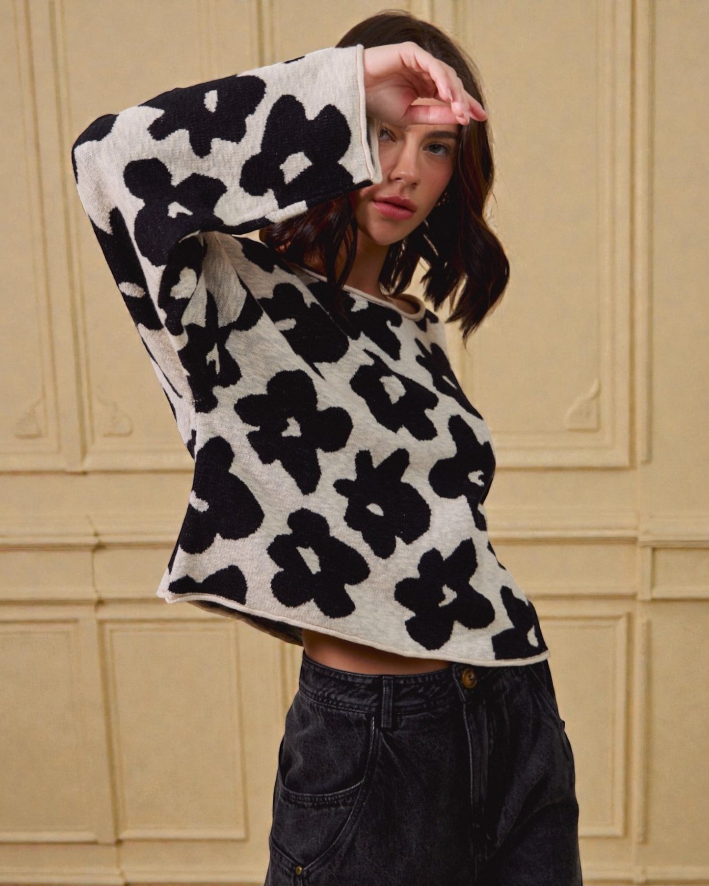 Person wearing a black and white floral patterned sweater against a beige wall.