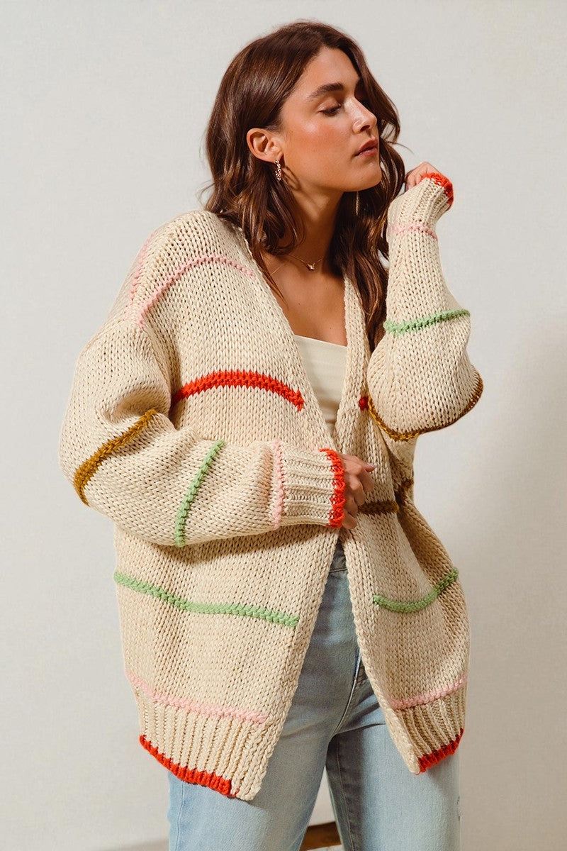 Woman wearing a cream-colored cardigan with colorful trim against a plain background