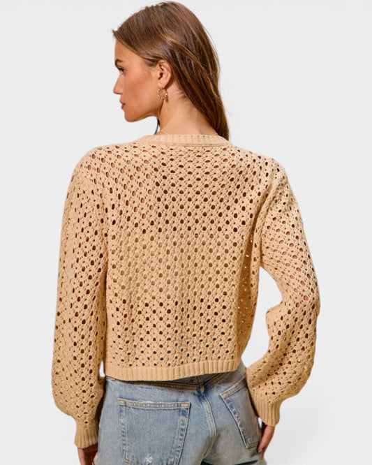 Woman wearing a beige open-knit sweater and jeans on a light gray background