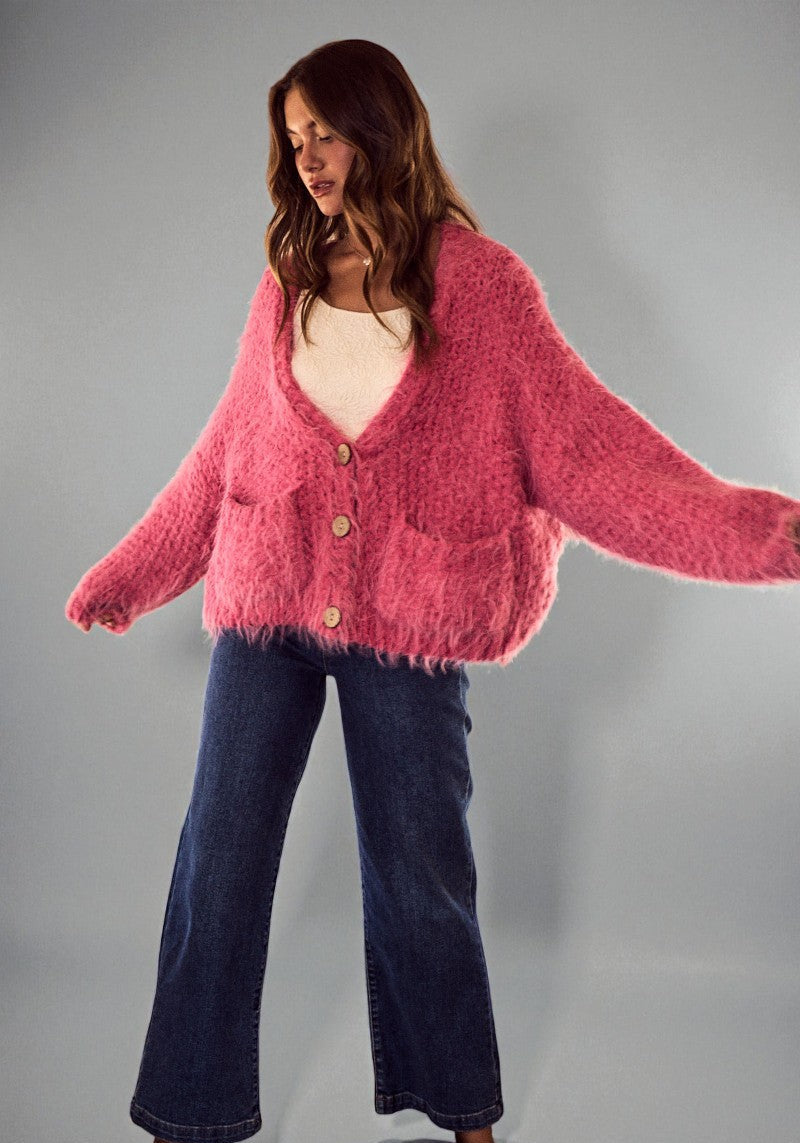 Woman wearing a pink cardigan and blue jeans against a gray background