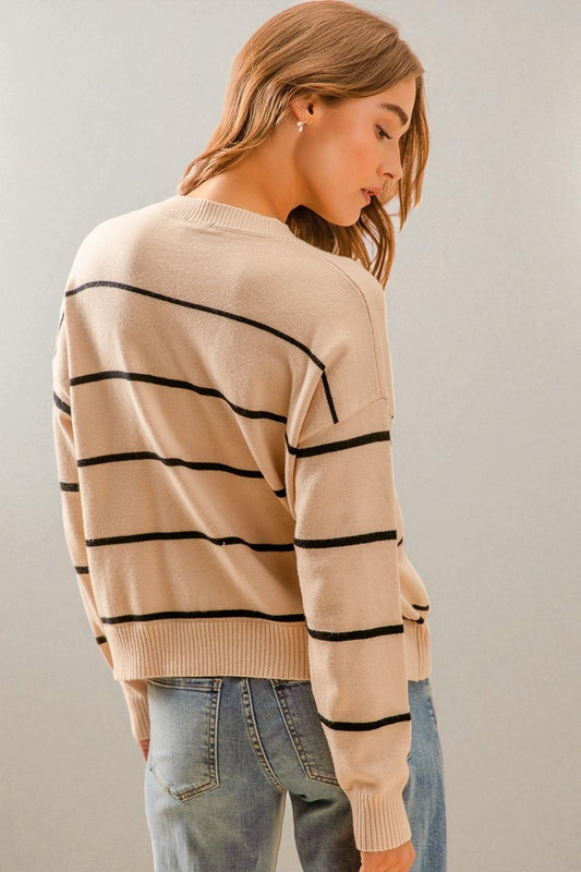 Woman wearing a beige sweater with black stripes and blue jeans against a plain background