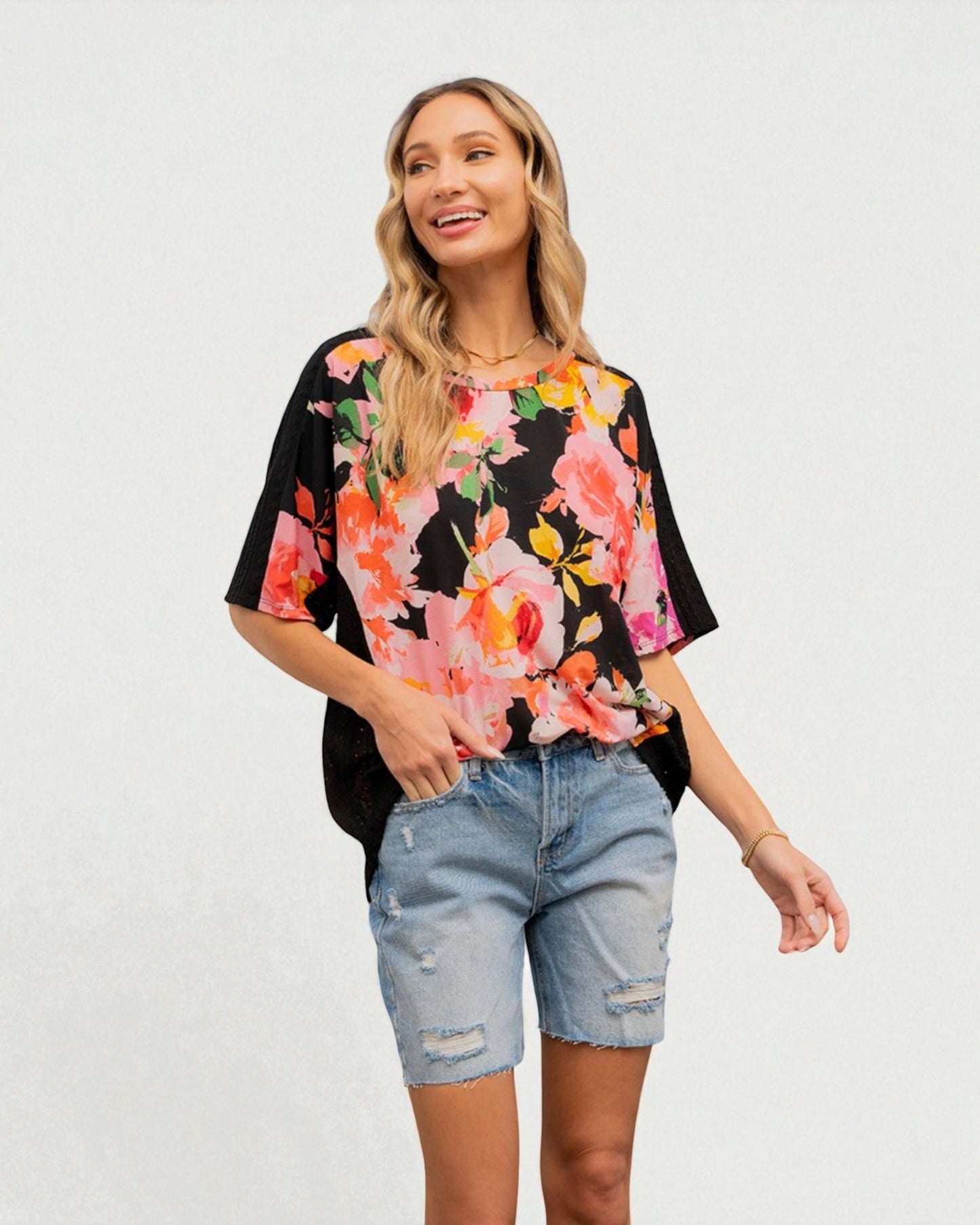 Woman wearing a floral blouse and denim shorts on a plain background