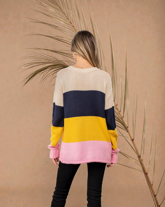Woman wearing a color-blocked sweater with a beige, navy, yellow, and pink design against a beige background.