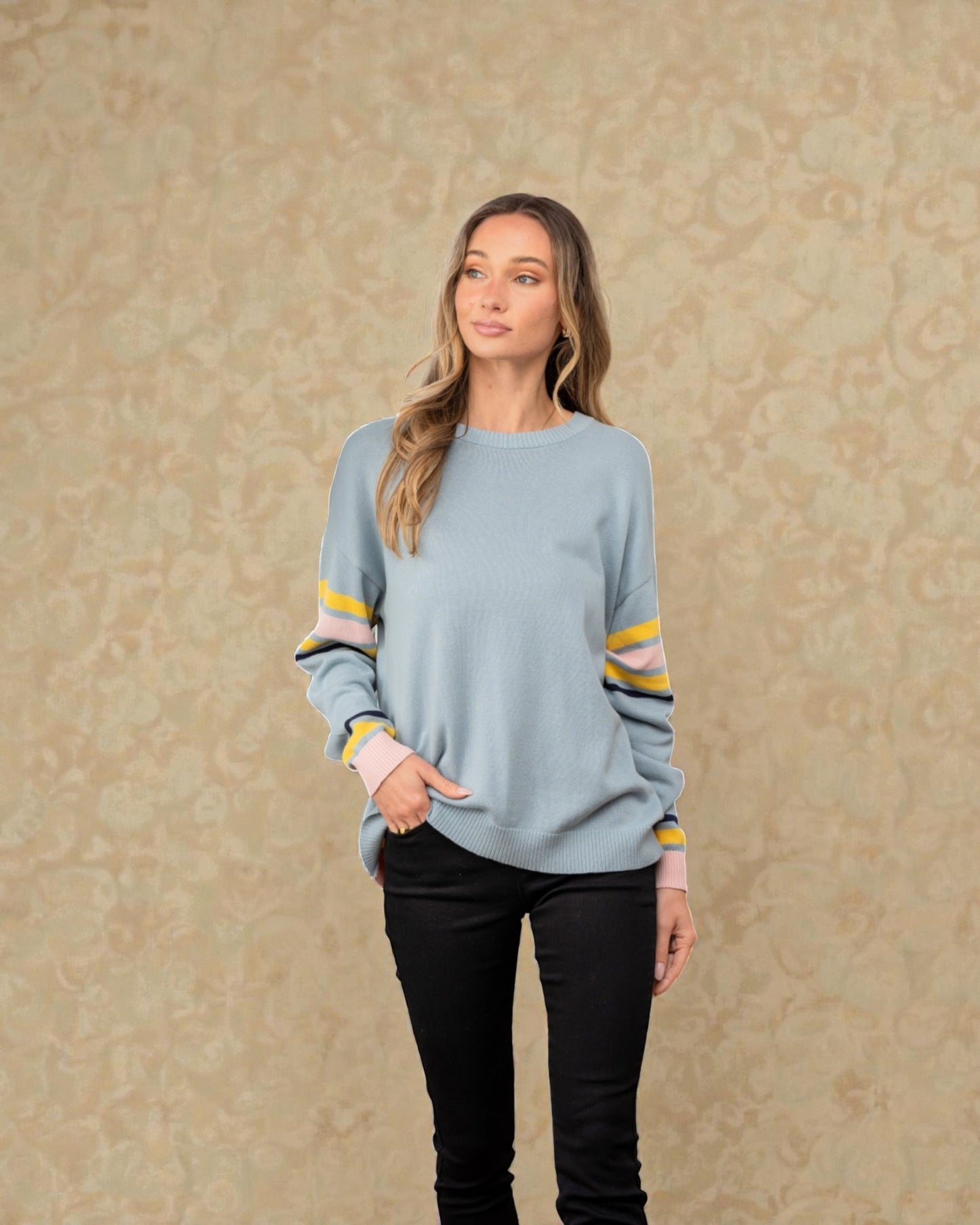 Woman wearing a light blue sweater with colorful sleeves against a beige background