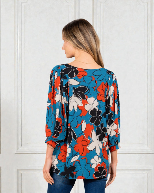 Woman wearing a colorful floral blouse against a white paneled wall