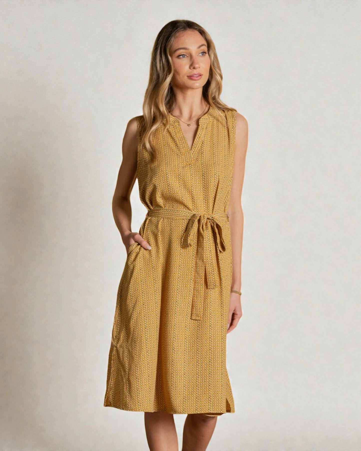 Woman wearing a mustard yellow dress with a belt against a plain background