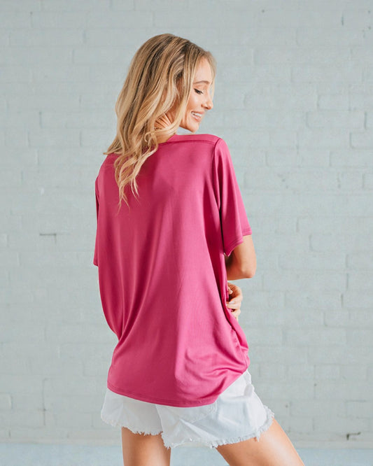 Woman wearing a pink oversized shirt and white shorts against a gray brick wall.