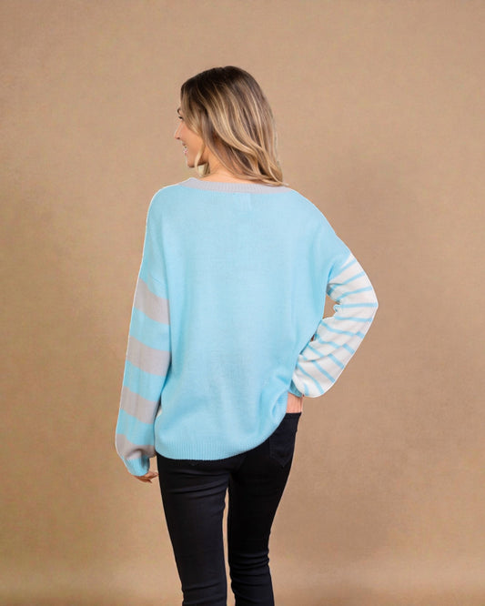 Woman wearing a light blue sweater with striped sleeves against a beige background