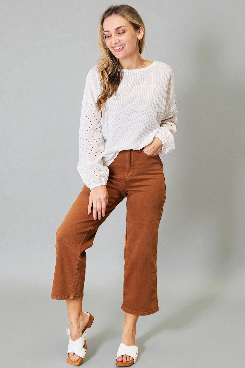 Woman wearing a white blouse and brown pants against a gray background