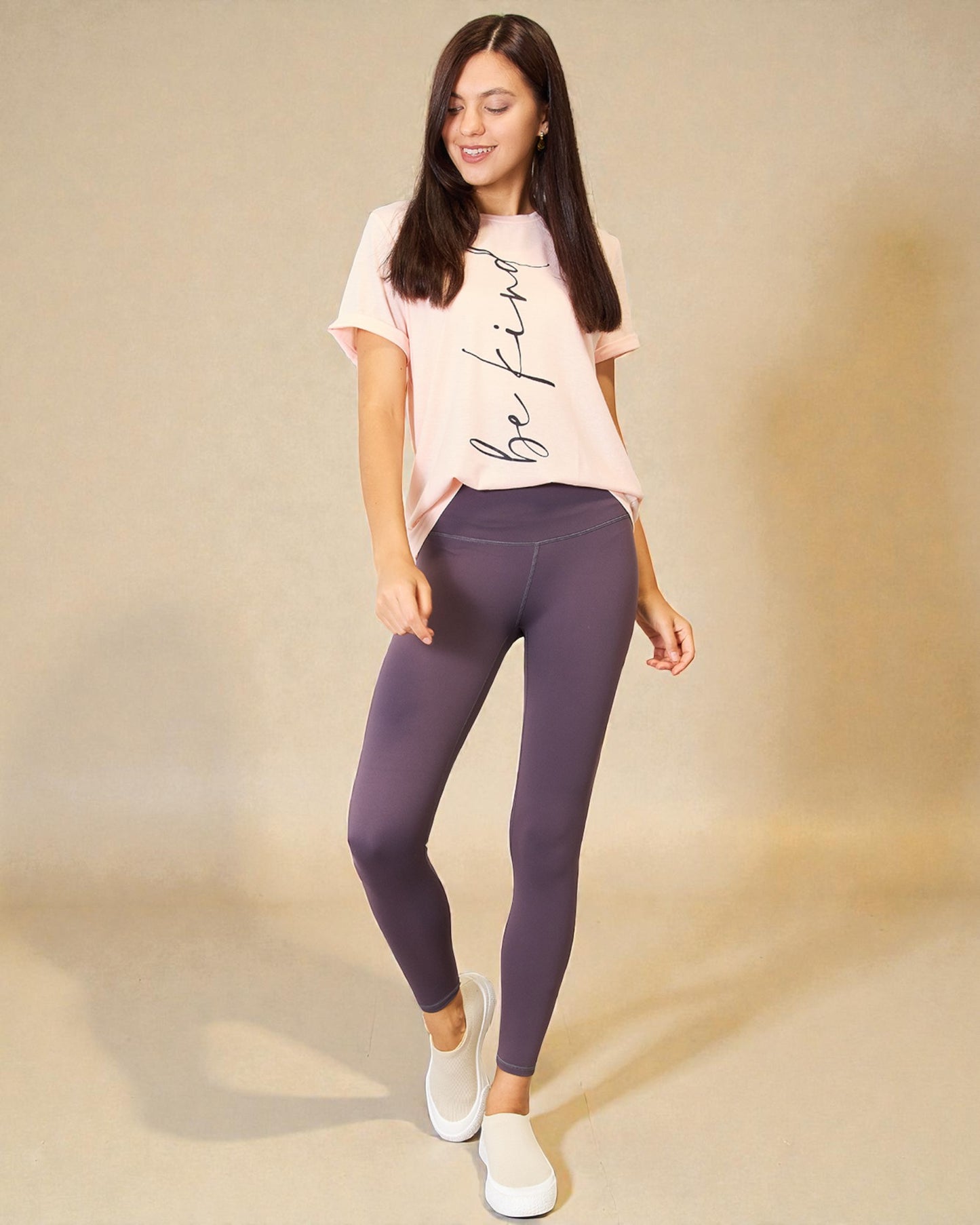 Woman wearing a pink t-shirt and purple leggings on a beige background