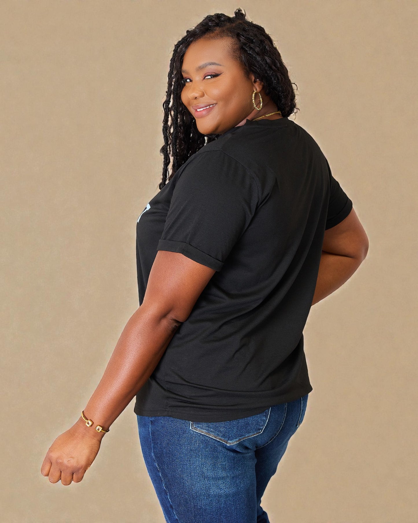 Woman wearing a black t-shirt and blue jeans against a beige background