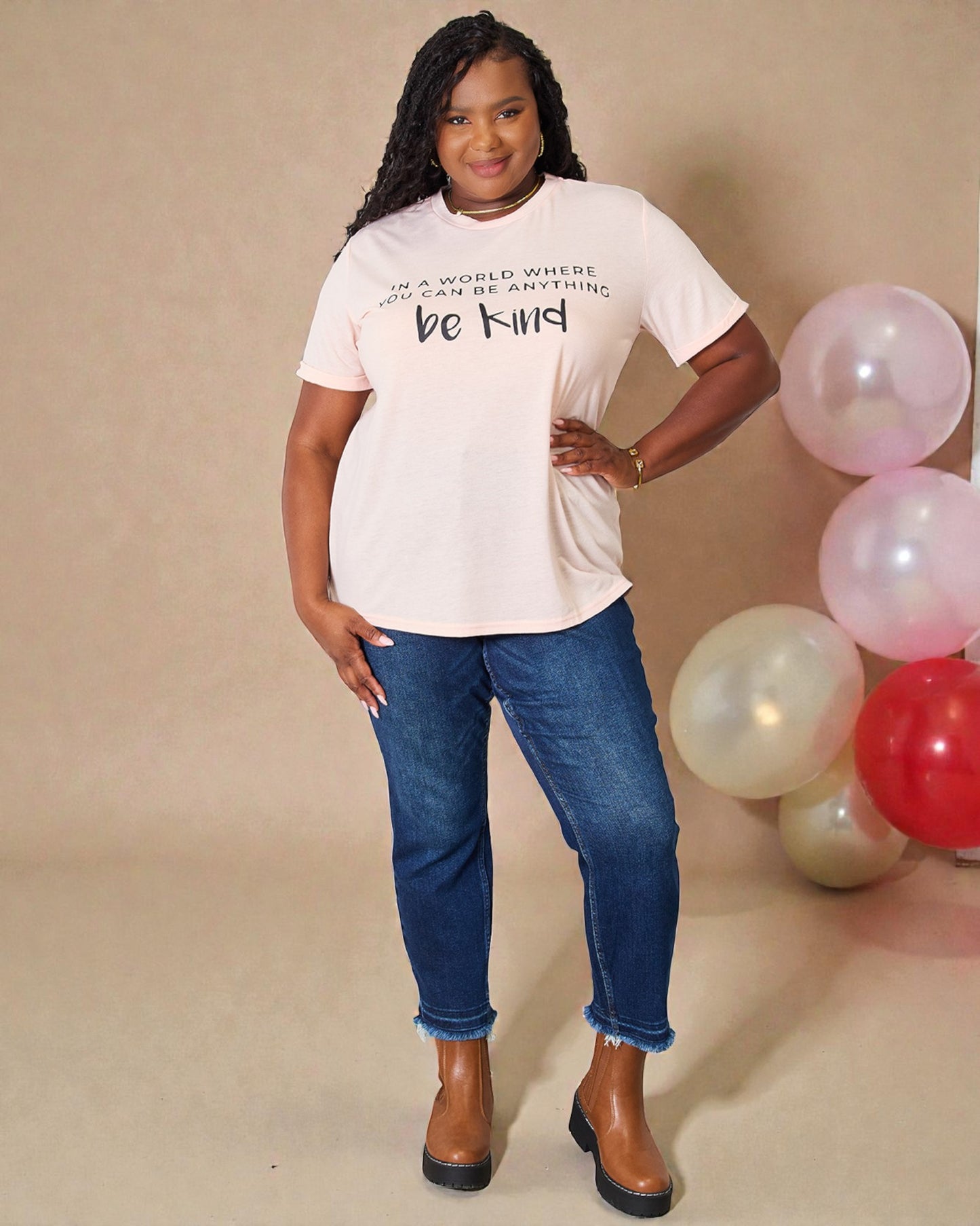 Woman wearing a white t-shirt with text and blue jeans, standing next to balloons on a beige background