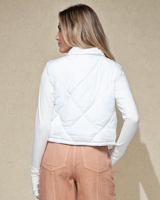 Woman wearing a white quilted jacket and beige pants against a beige background