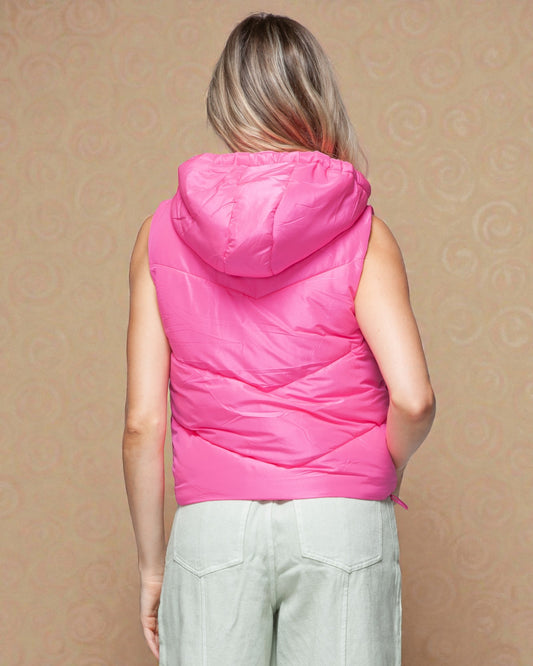 Person wearing a pink puffer vest against a beige wall