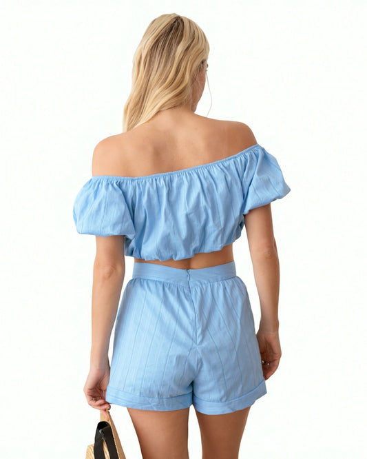 Woman wearing a light blue off-shoulder top and shorts set on a white background