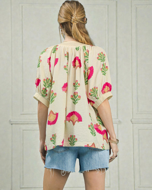 Woman wearing a floral blouse and denim shorts against a light gray wall.