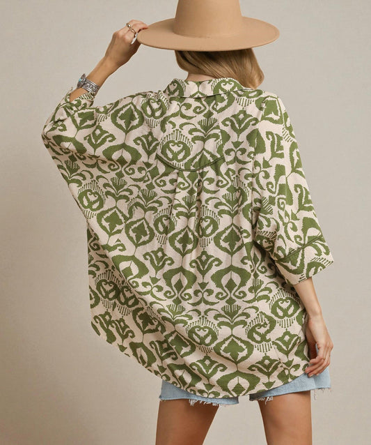 Person wearing a green and beige patterned shirt with a beige hat on a plain background