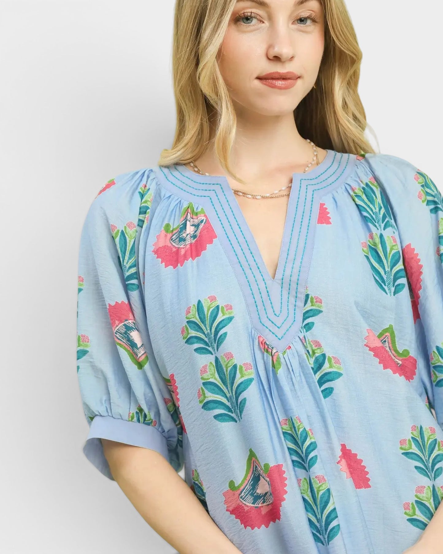Woman wearing a light blue dress with colorful floral patterns on a plain background
