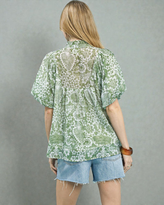 Person wearing a green floral blouse and denim shorts on a gray background