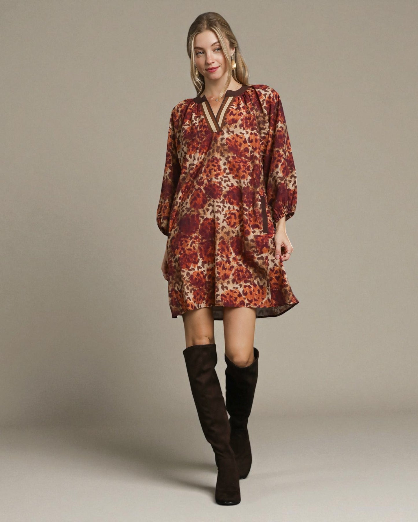 Woman wearing a patterned dress and knee-high boots on a plain background