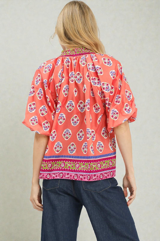 Woman wearing a red patterned blouse with blue pants on a plain background