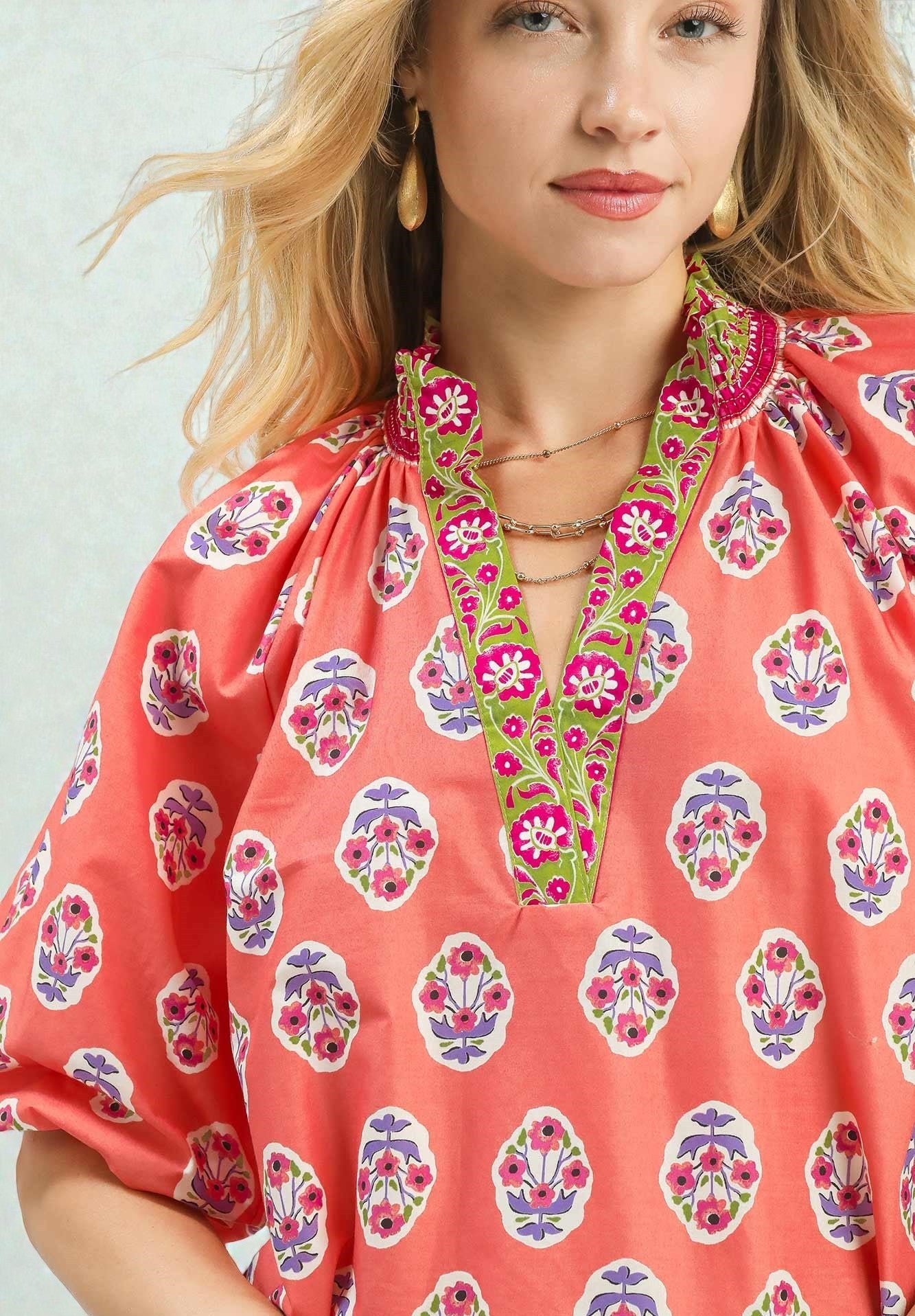 Woman wearing a coral blouse with colorful floral patterns on a white background