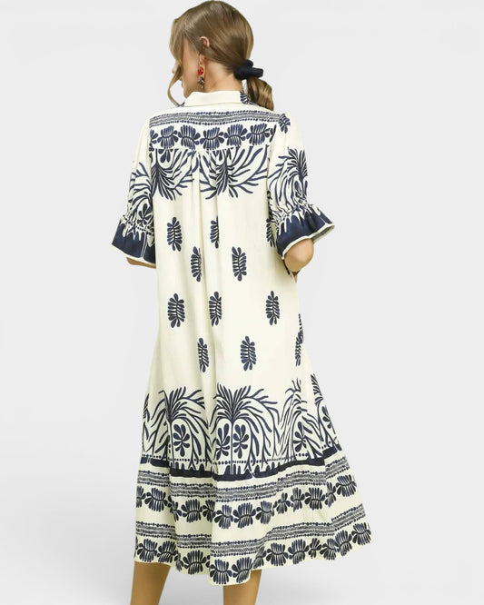 Woman wearing a white dress with black floral patterns on a plain background