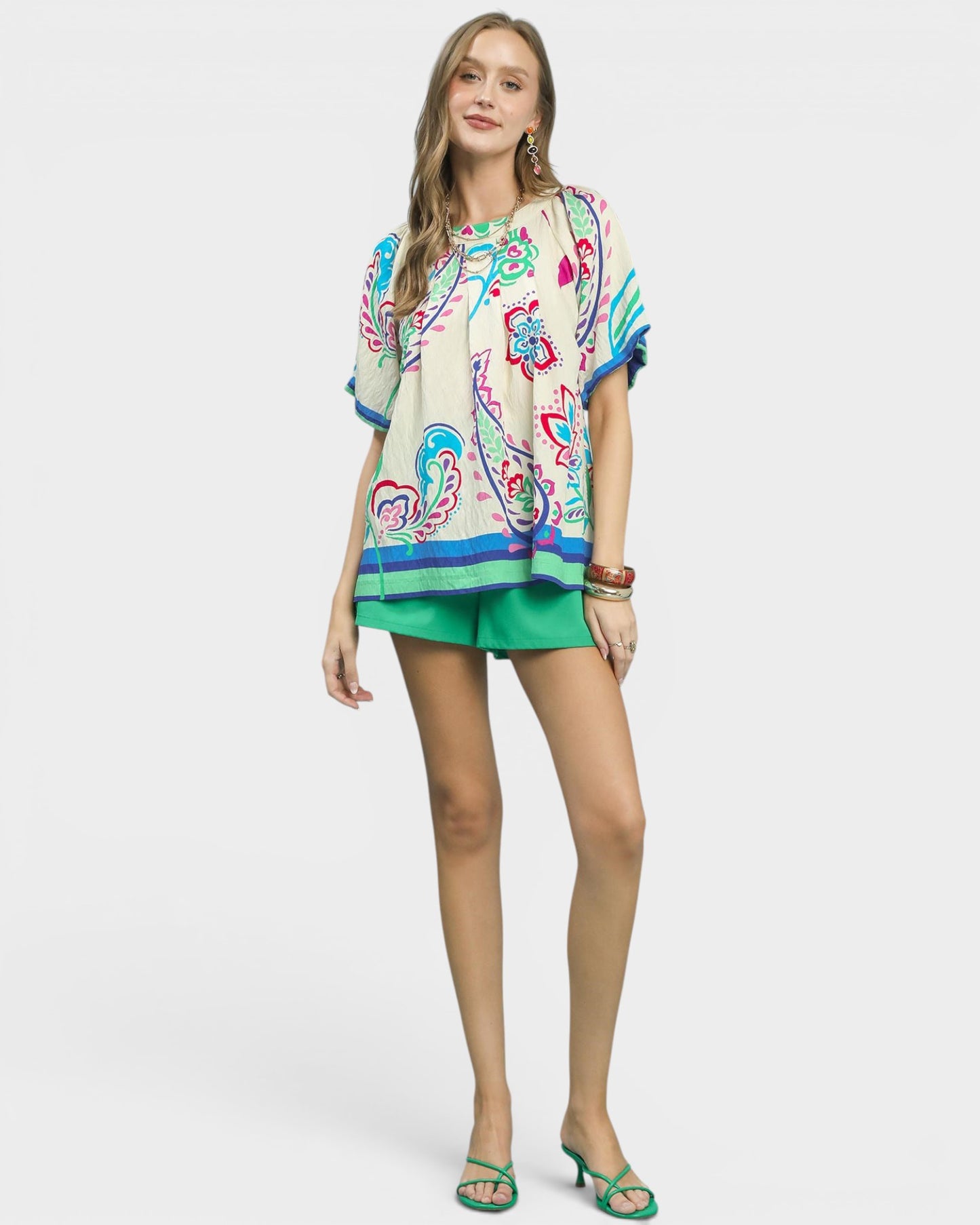 Woman wearing a colorful patterned top and green shorts on a white background