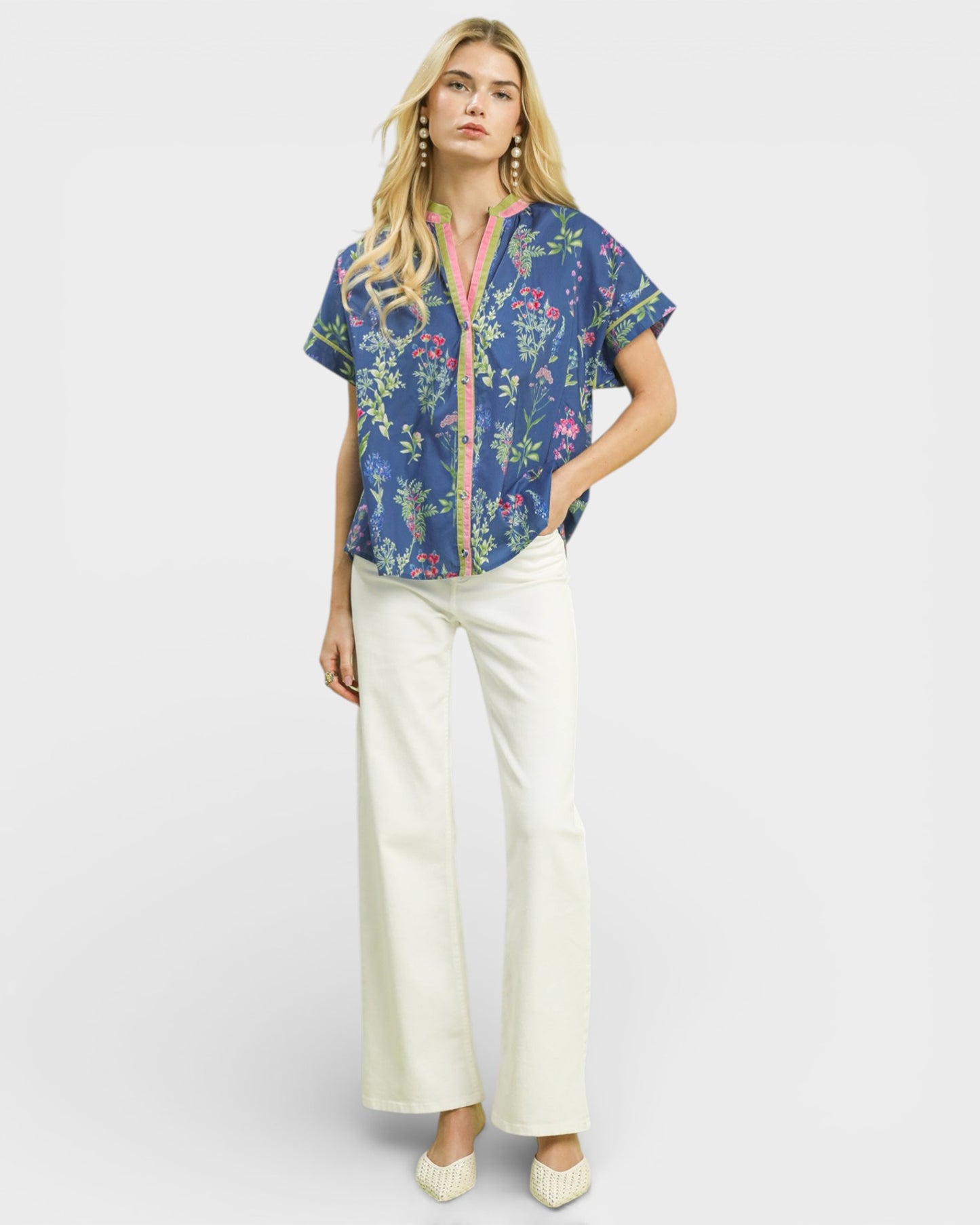 Woman wearing a colorful floral blouse and white pants on a white background