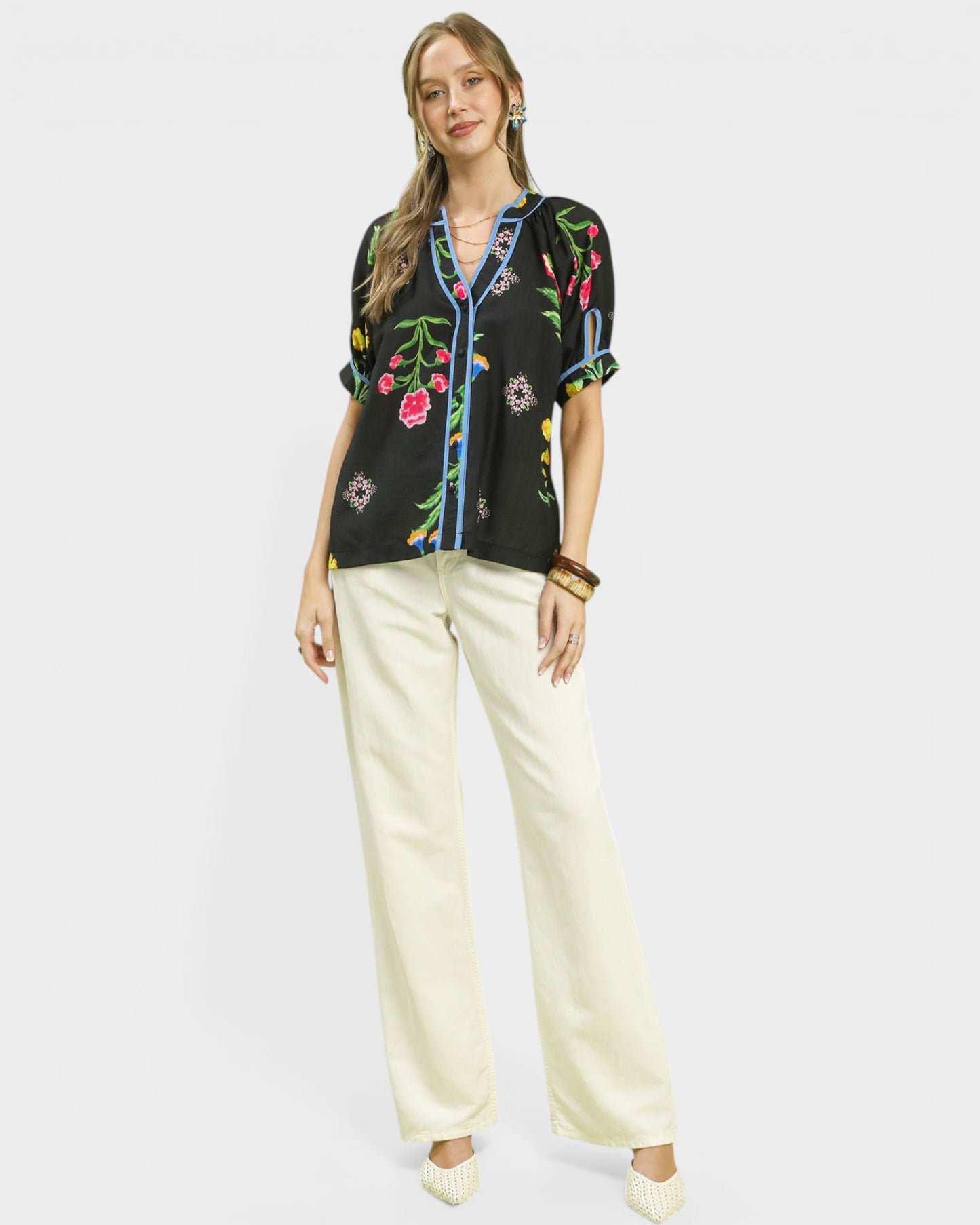 Woman wearing a black embroidered blouse with colorful designs and white pants on a light gray background