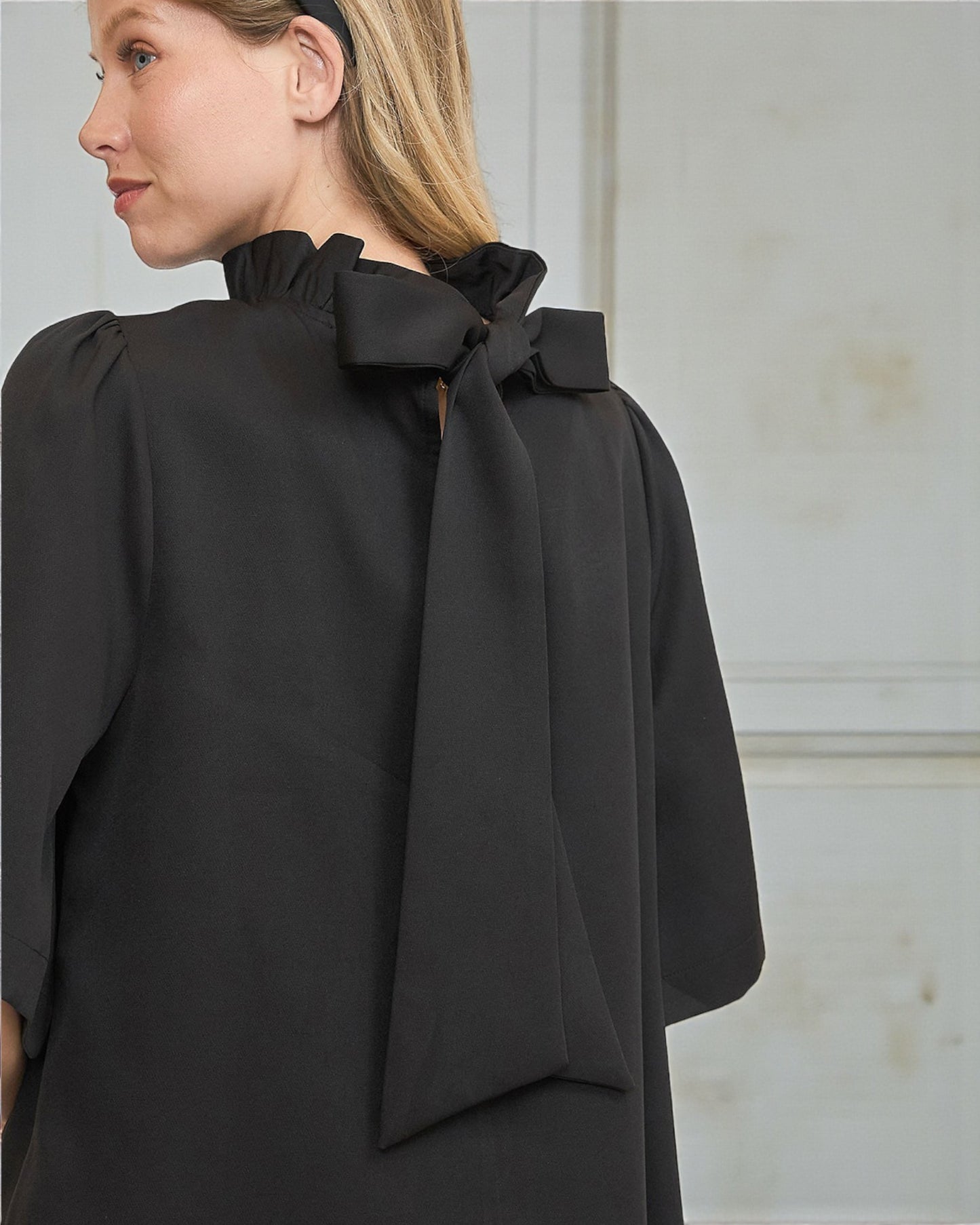 Woman wearing a black blouse with a large bow detail on a neutral background
